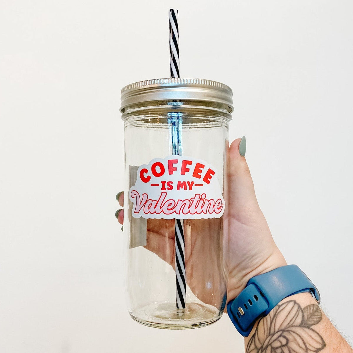 hand holding a mason jar tumbler that reads"coffee is my valentine" the first 3 words are in block letters and red. Valentine is in cursive and pink with a red outline