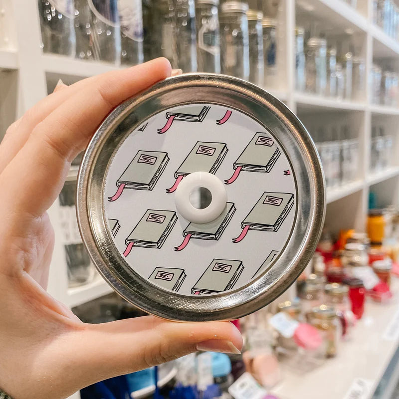 Hand holding mason jar patterned straw lid that has mint coloured books on light blue background 