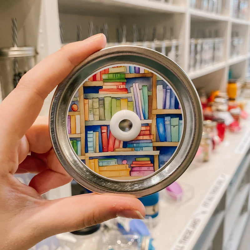 Hand holding mason jar patterned straw lid that has multicolour books 