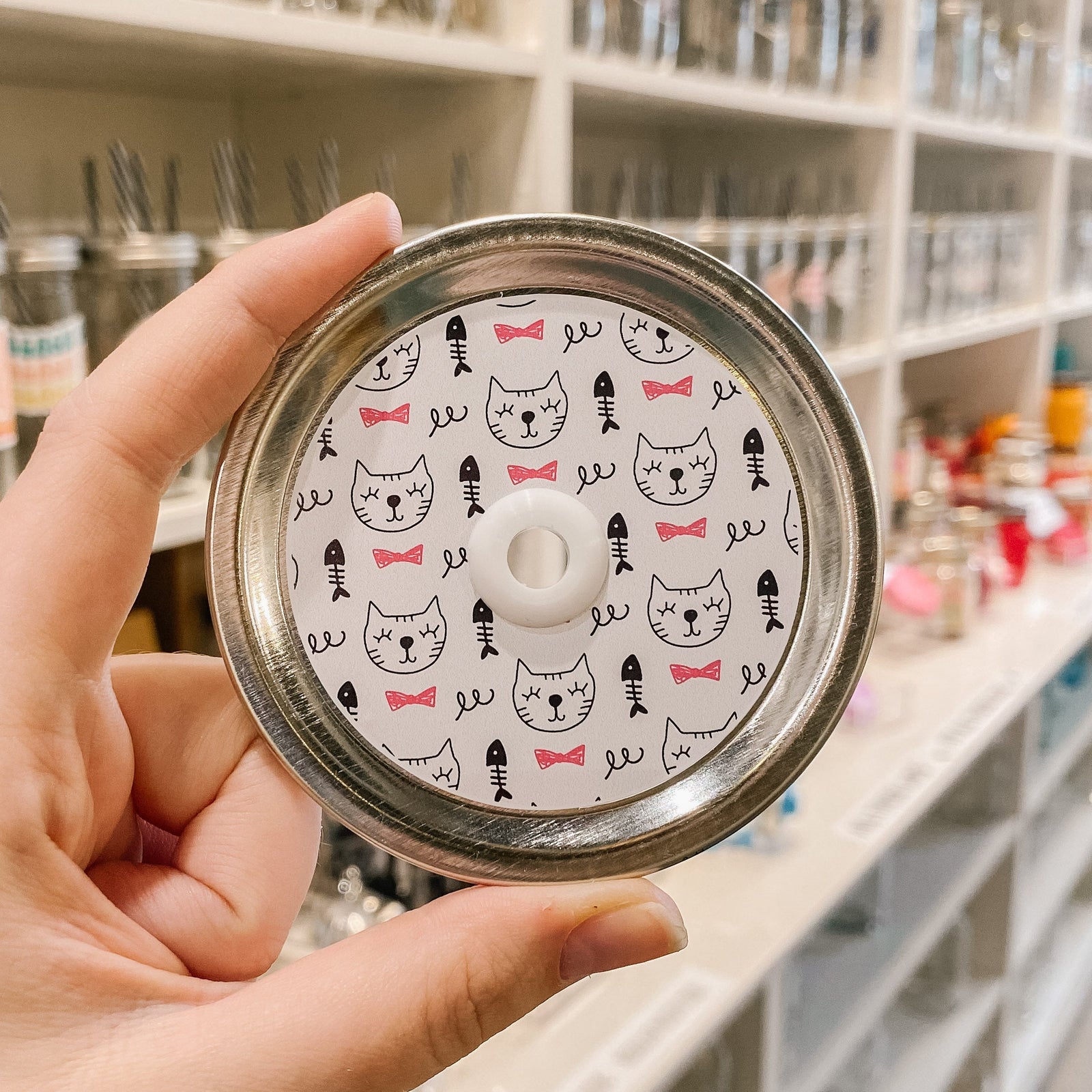 straw lid with white background, line drawings of cat faces, fish skeletons, and red bow ties
