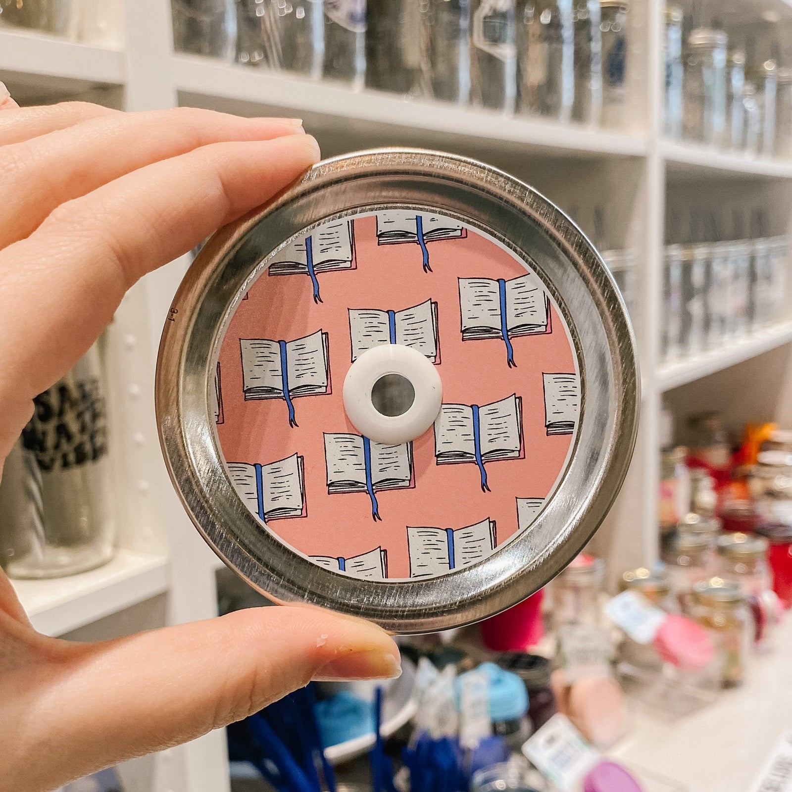 straw lid with light pink background, repeated pattern of an open book with a blue ribbon bookmark