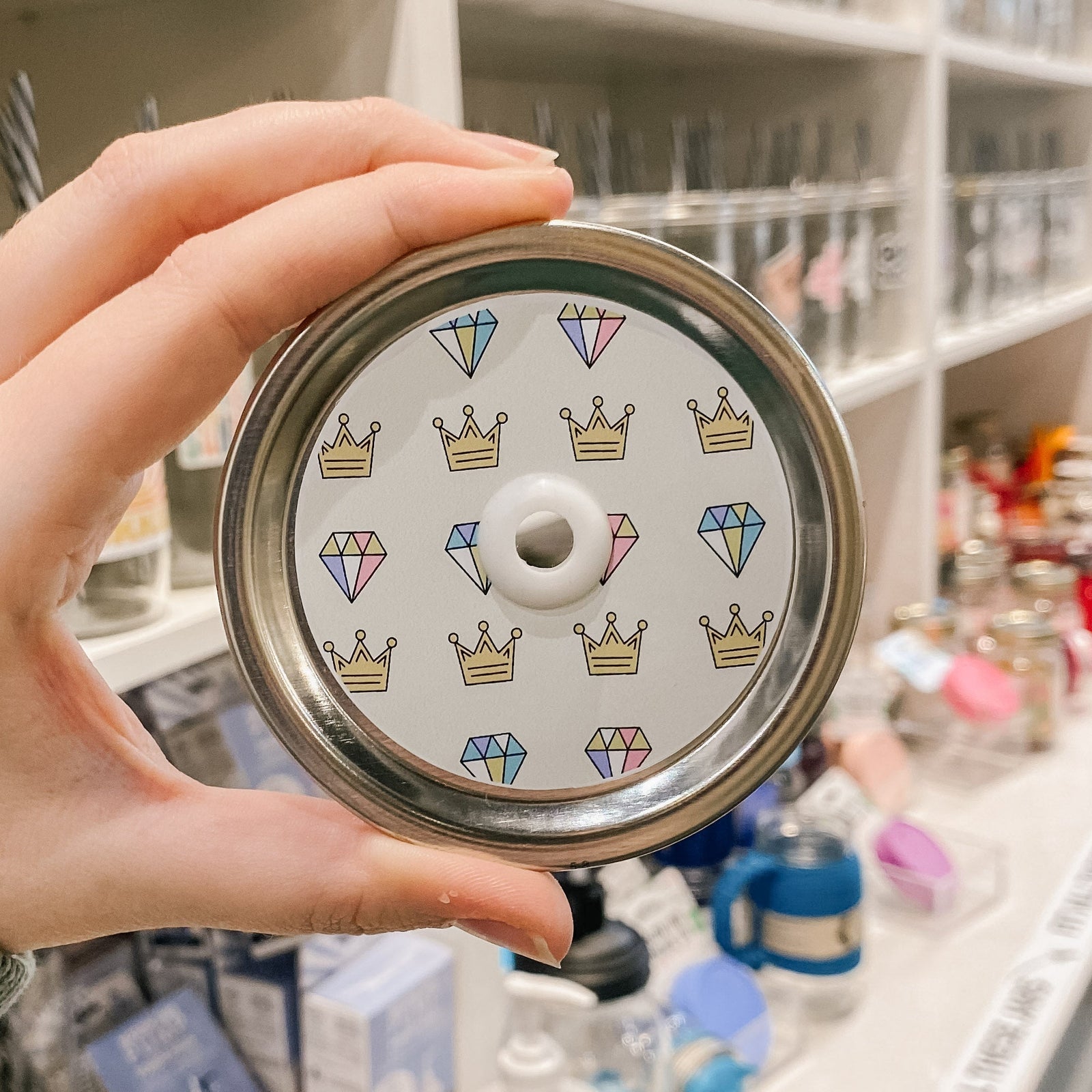 a straw lid with a taupe background, crowns, and diamonds patterned across