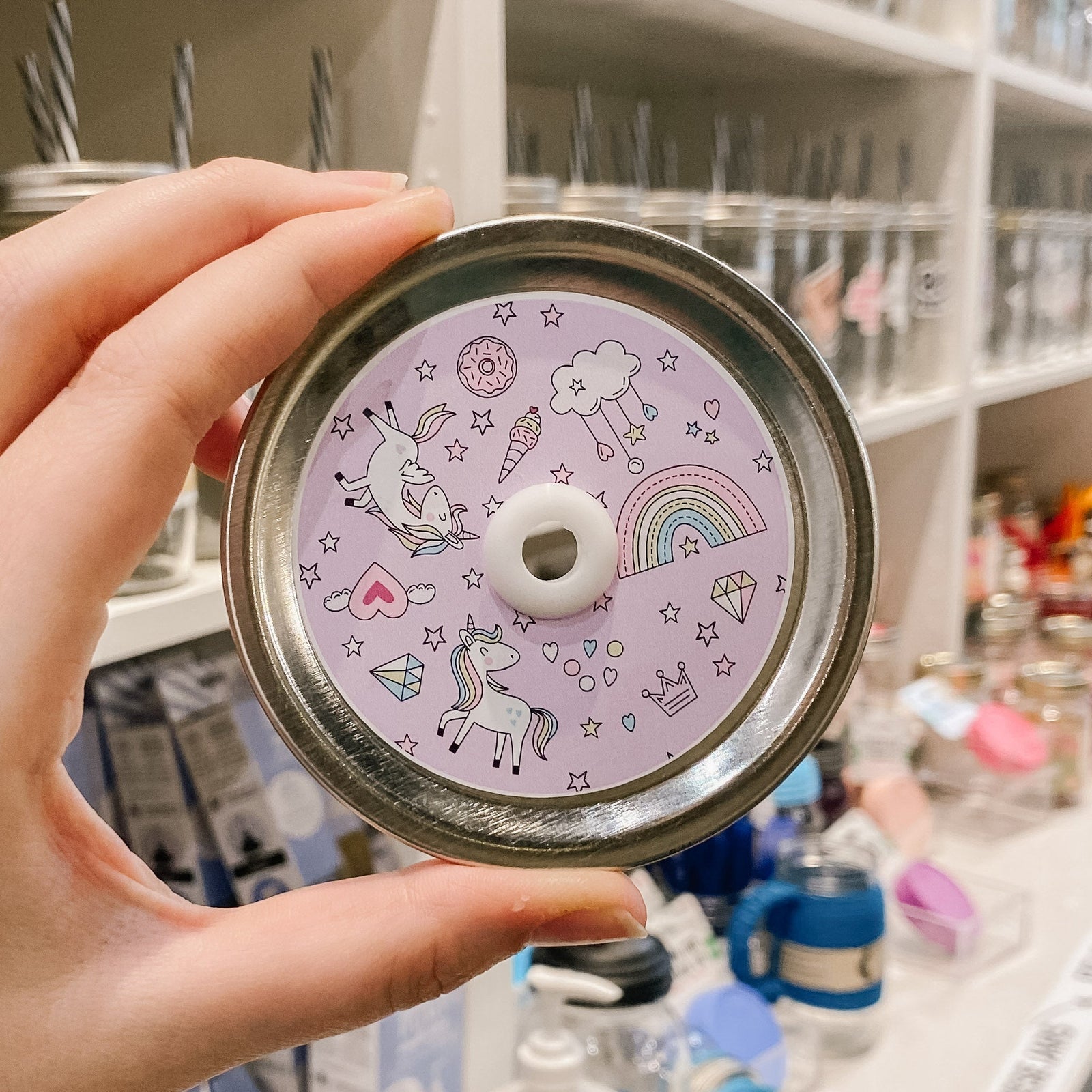 straw lid with a pink background with unicorns, rainbows clouds, diamonds, hearts, stars, donuts, and ice creams scattered around. 