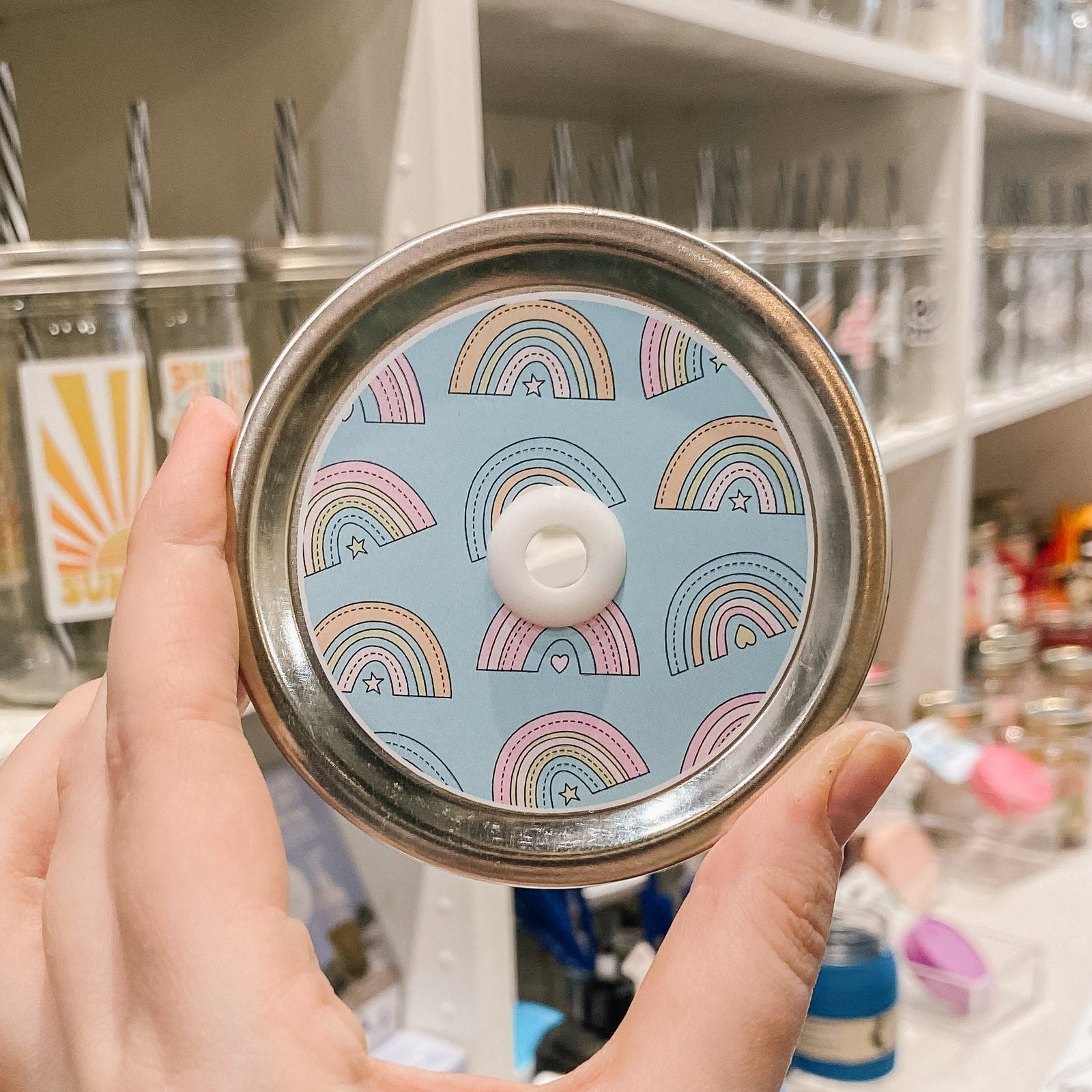 straw lid with a blue background with rainbows patterned across, each rainbow has a small star or heart underneath