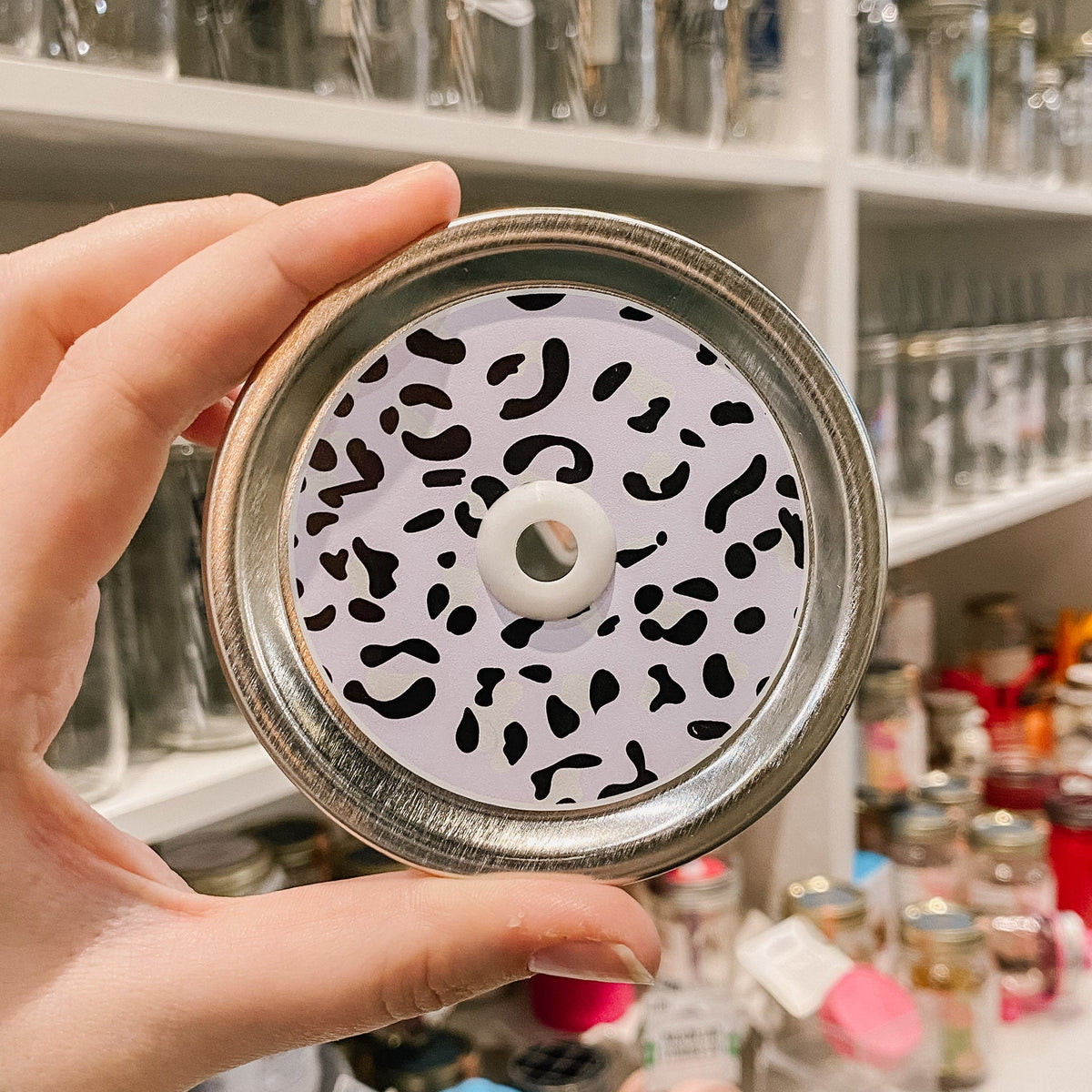 Hand holding a lavender leopard print patterned mason jar straw lid with white straw grommet