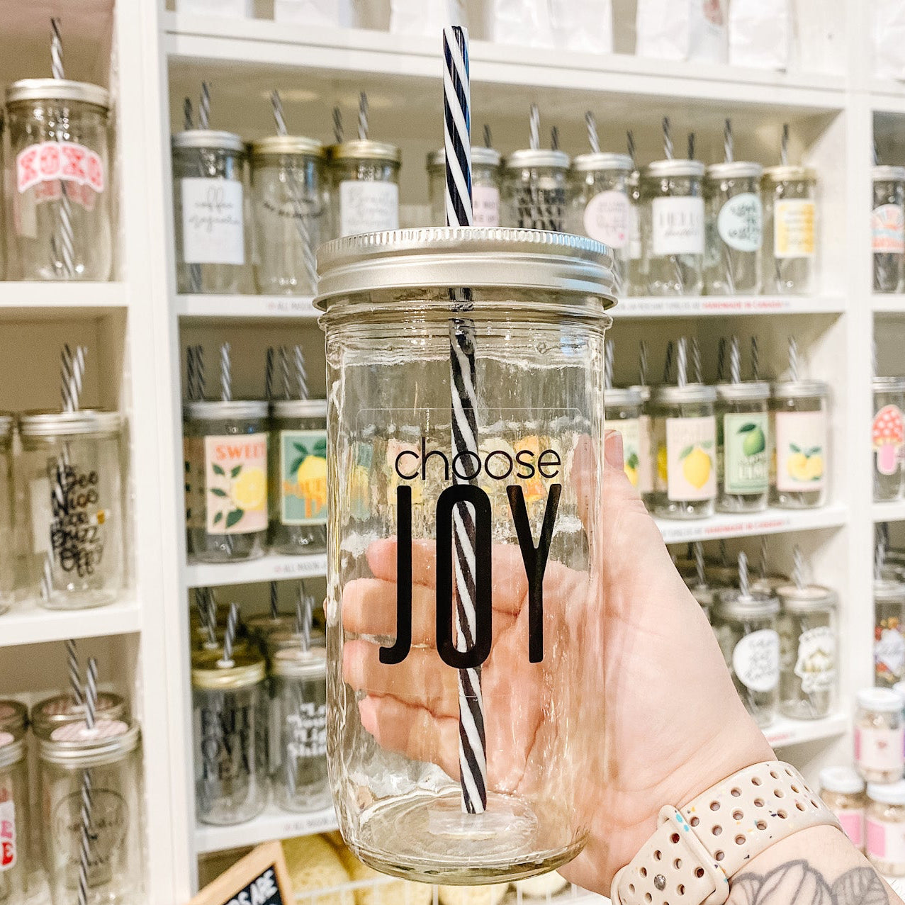 Hand holding a mason jar tumbler that reads choose joy in black text on clear background 