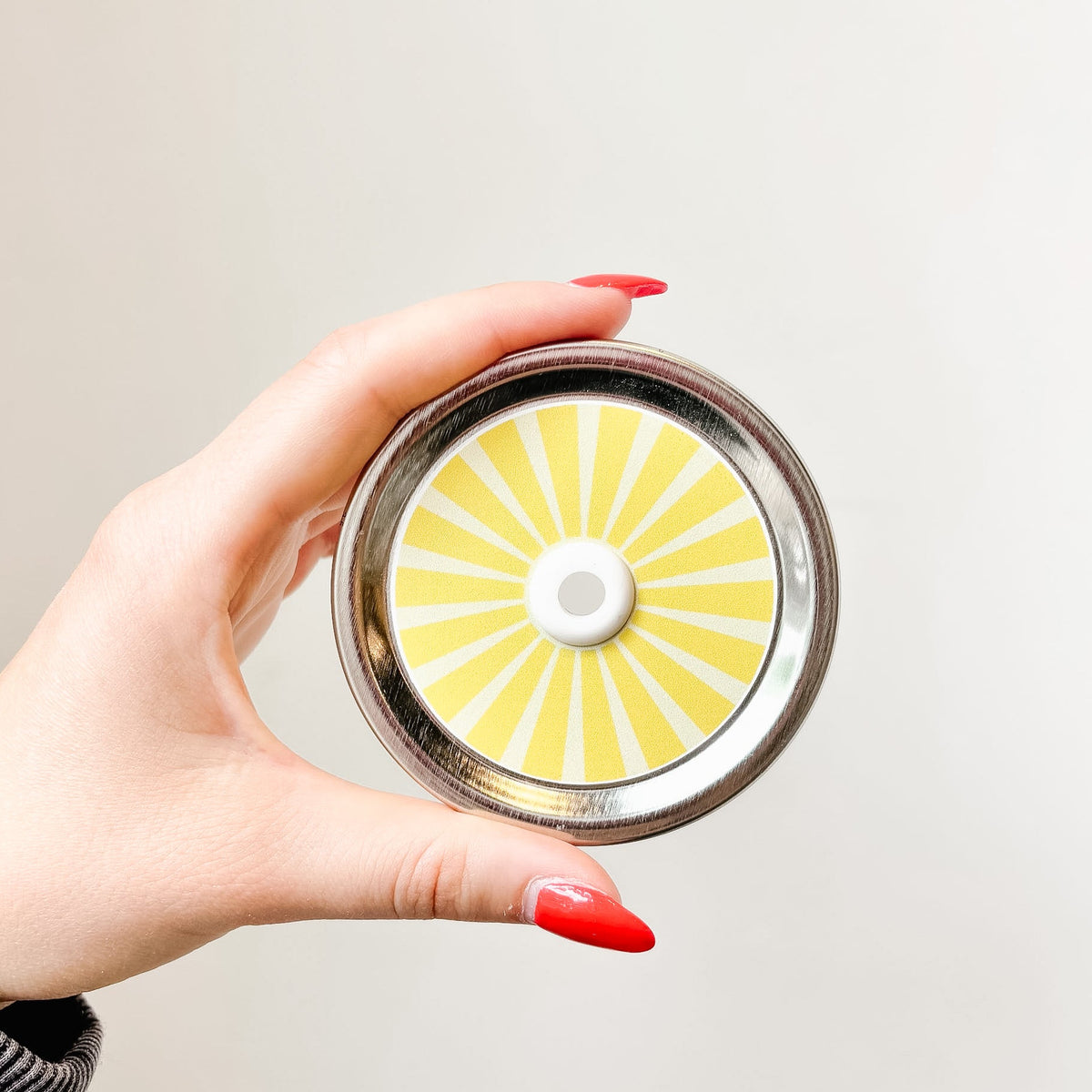 Hand holding a mason jar patterned straw lid that has yellow striped design 
