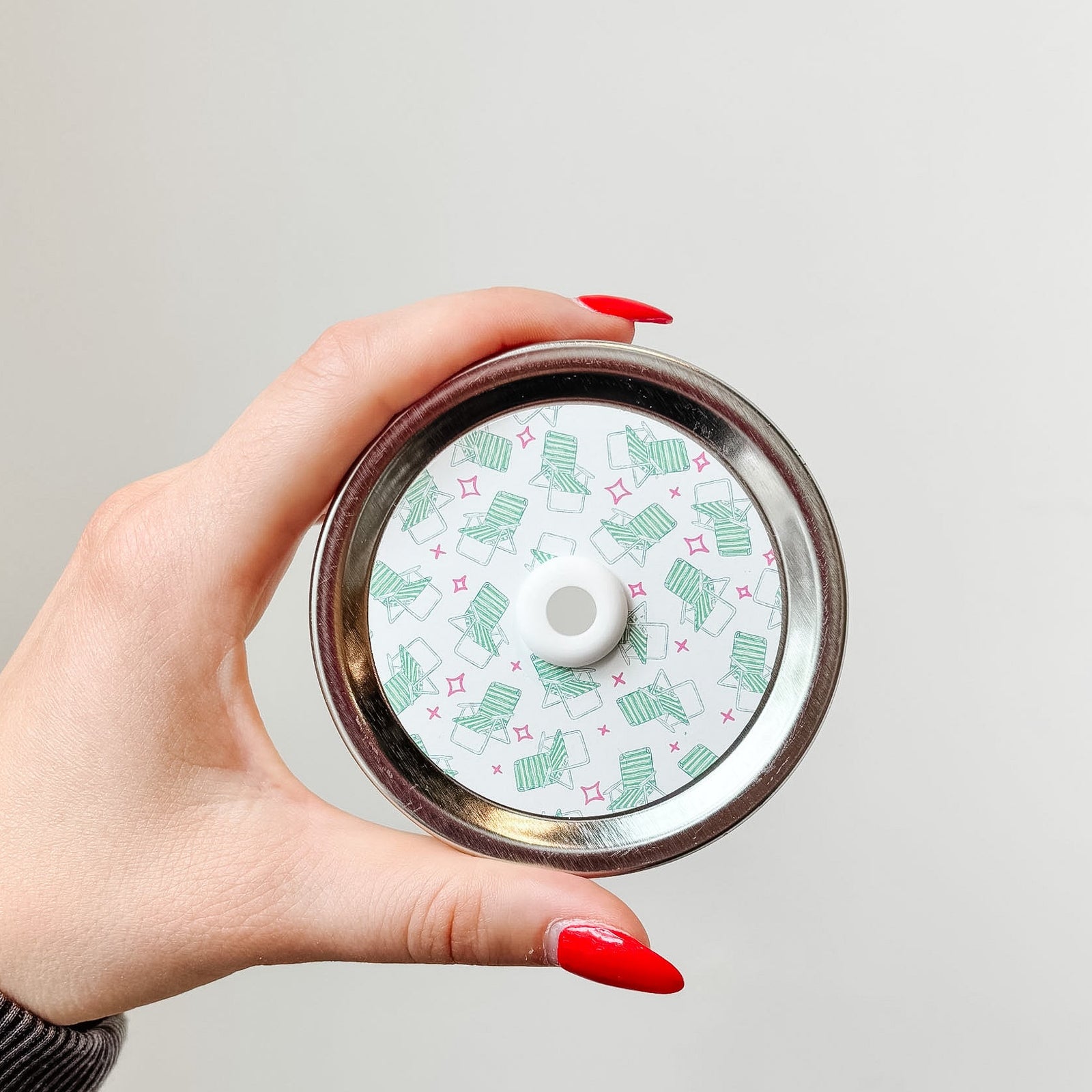 Hand holding mason jar patterned straw lid that has small green beach chairs and red stars on white background 