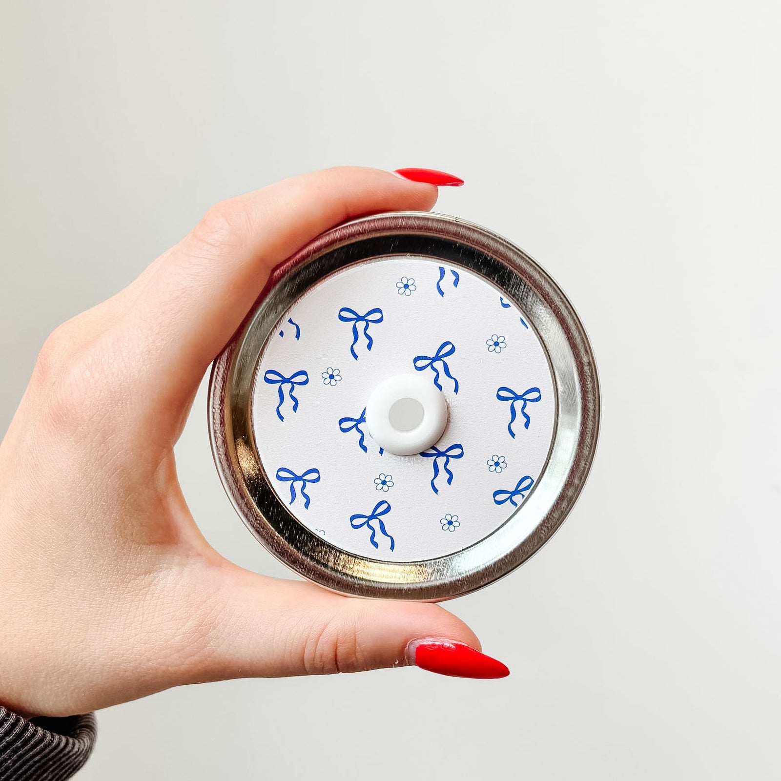 Hand holding a mason jar patterned straw lid that has blue bows and flowers on white background 