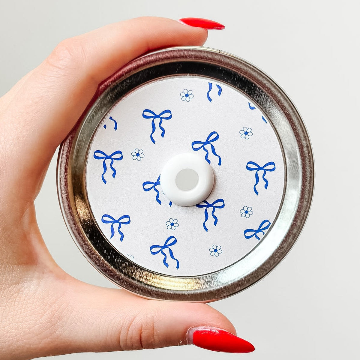 Hand holding a mason jar patterned straw lid up close that has blue bows and flowers on white background
