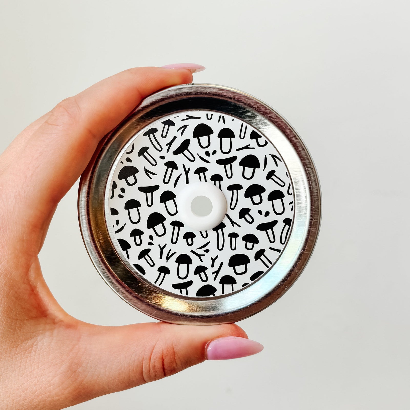 Hand holding mason jar patterned straw lid that  has black and white shaped mushroom designs on white background