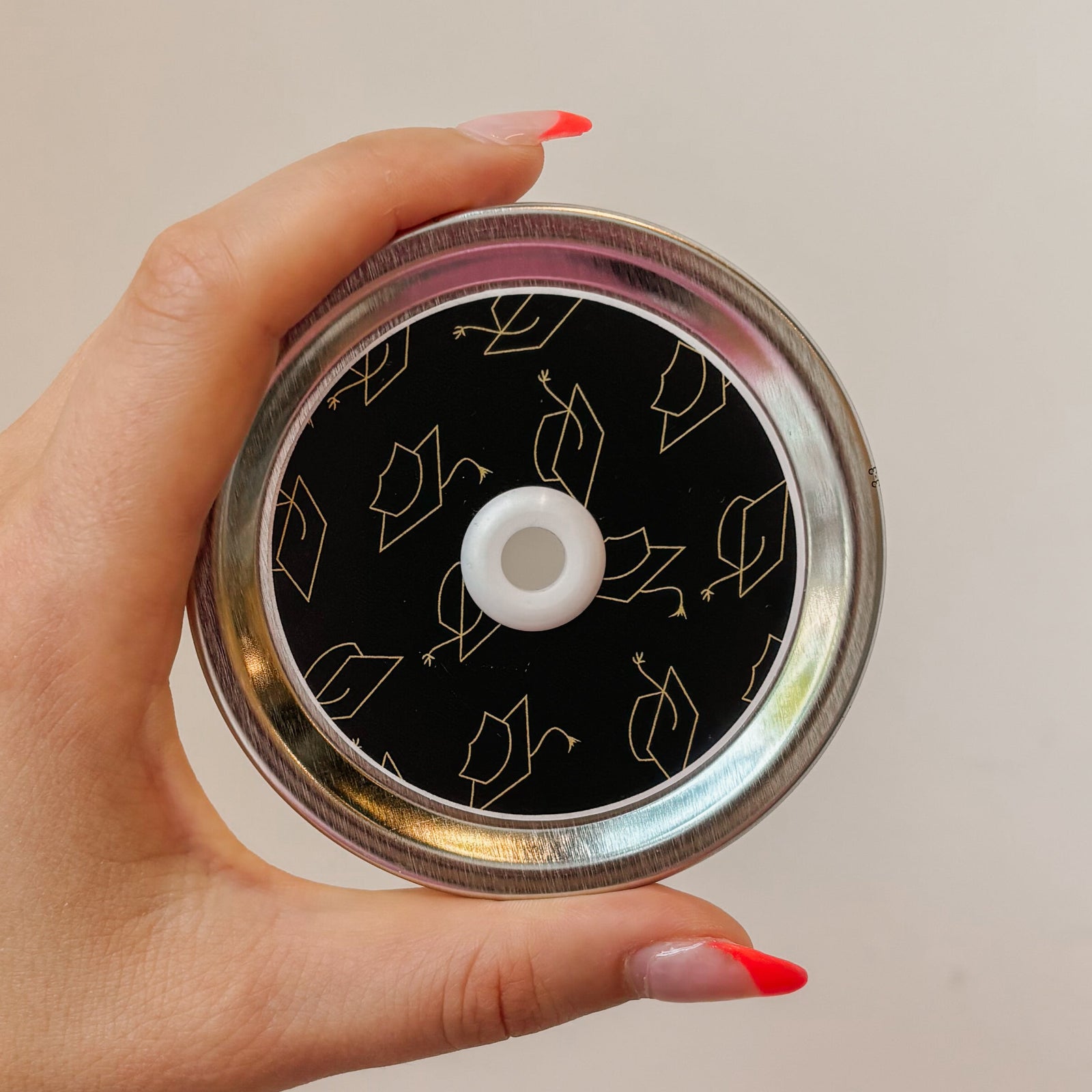 Hand holding mason jar patterned straw lid hat has gold grad caps on black background