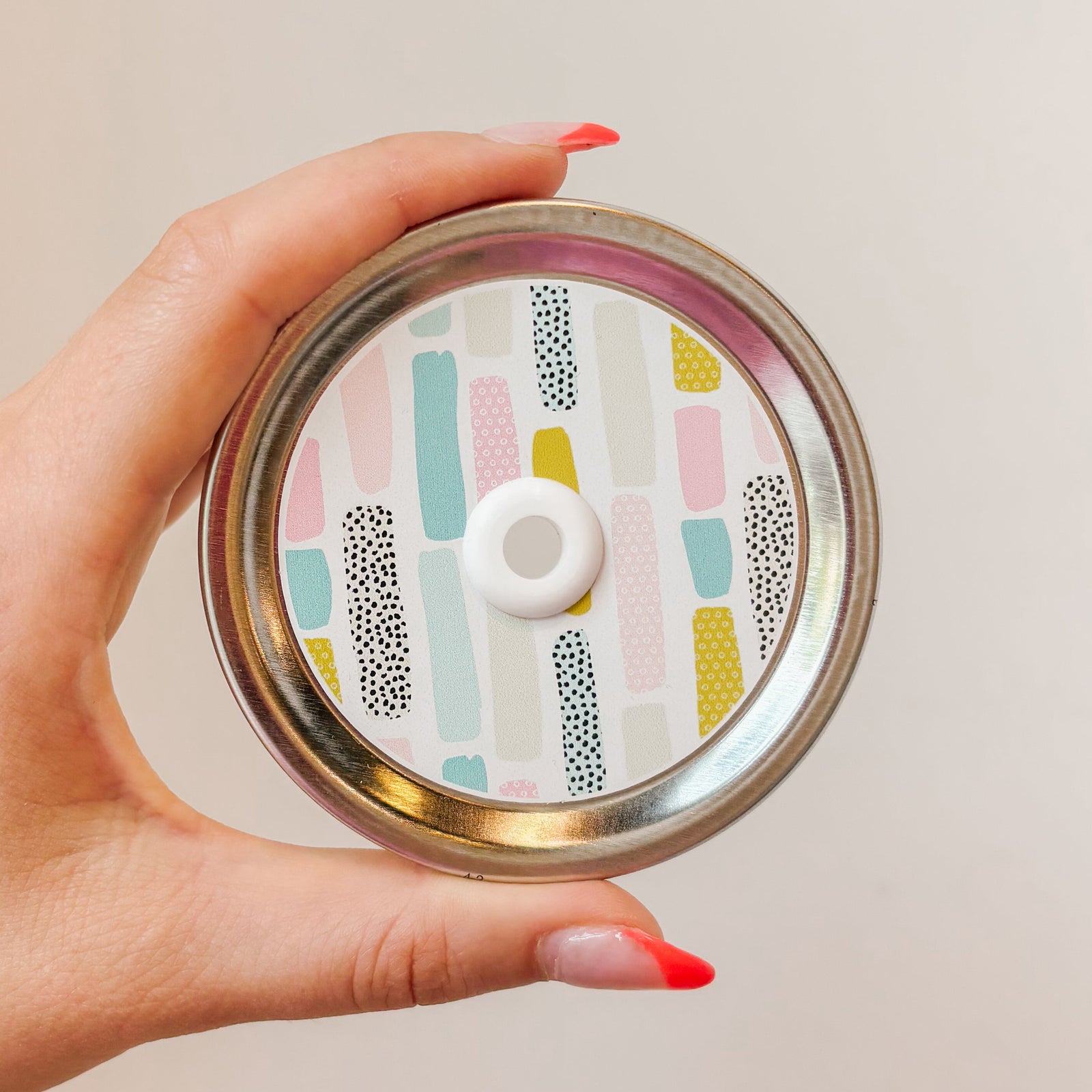 Hand holding mason jar patterned straw lid that has pastel strips on white background
