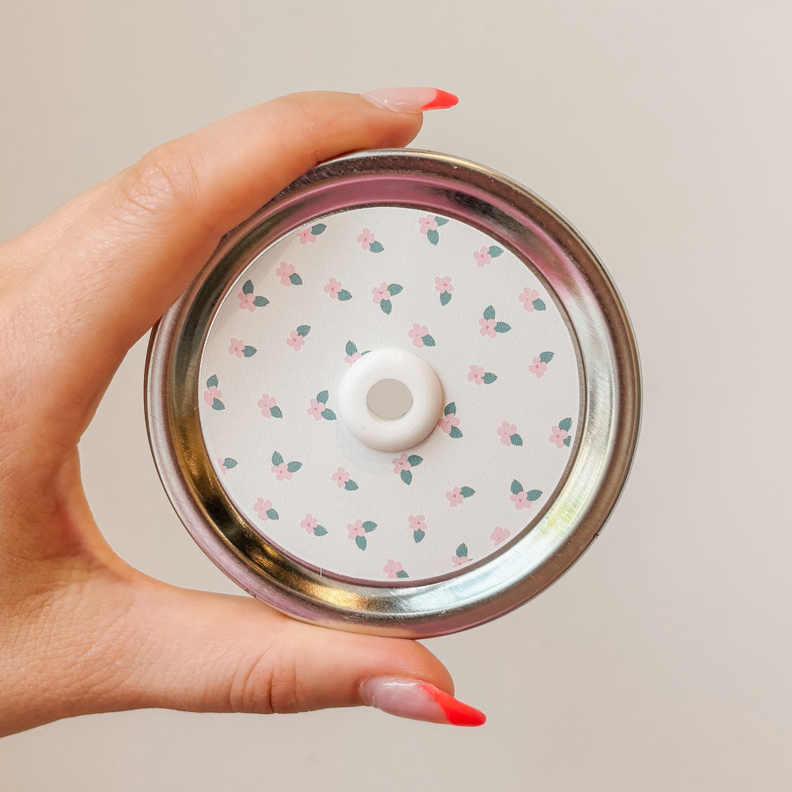 Hand holding mason jar patterned straw lid that has tiny pink flowers on off white background