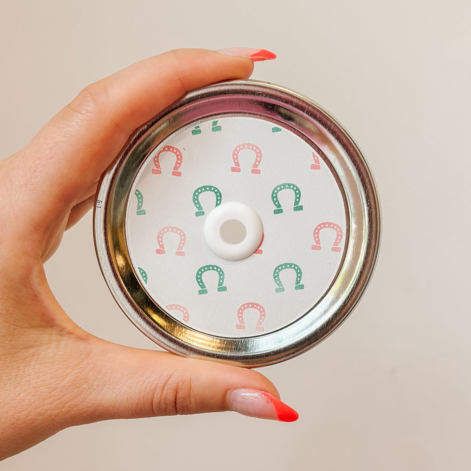 Hand holding mason jar patterned straw lid that has green and pink horseshoes on a white background.