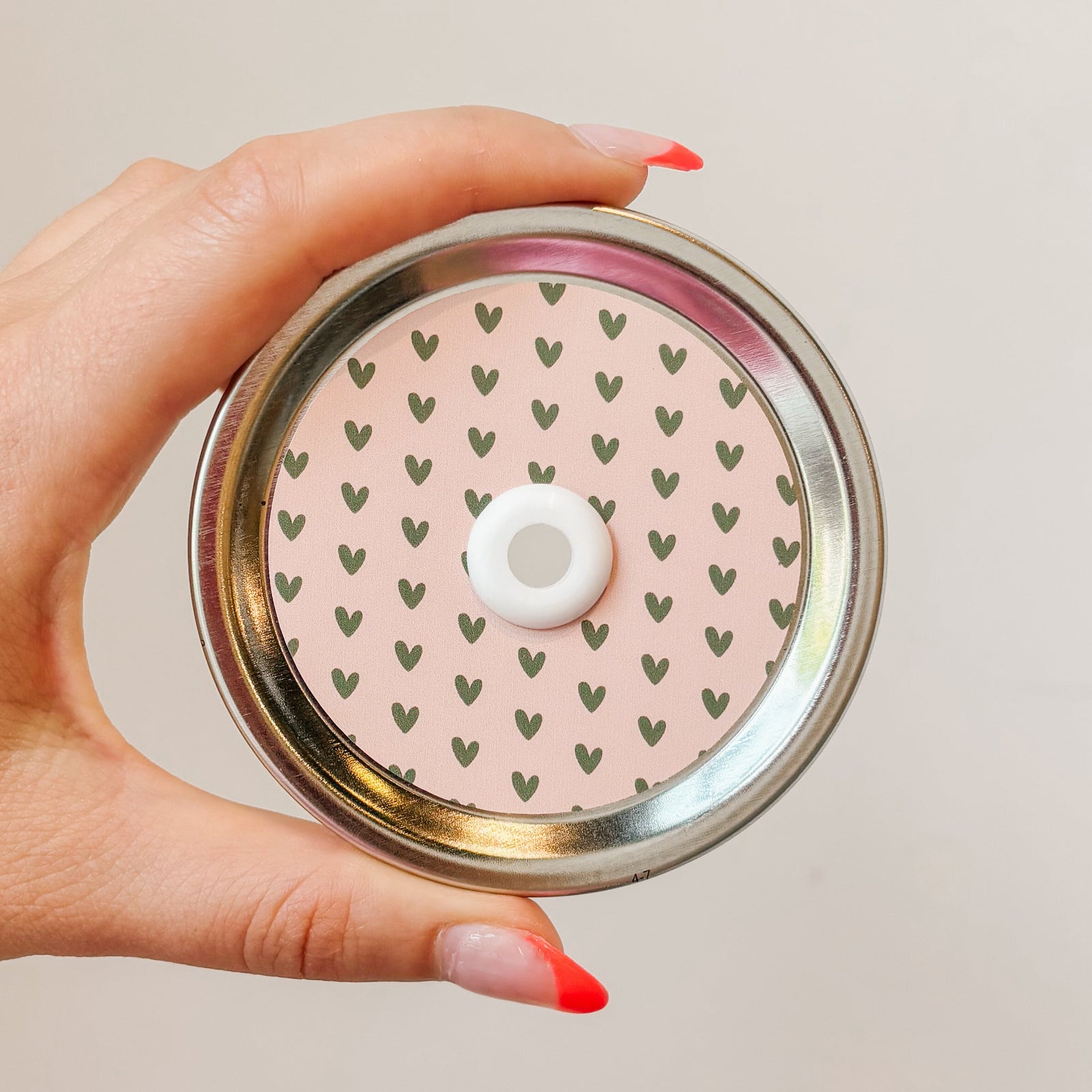 Hand holding mason jar patterned straw lid with green hearts on blush pink background