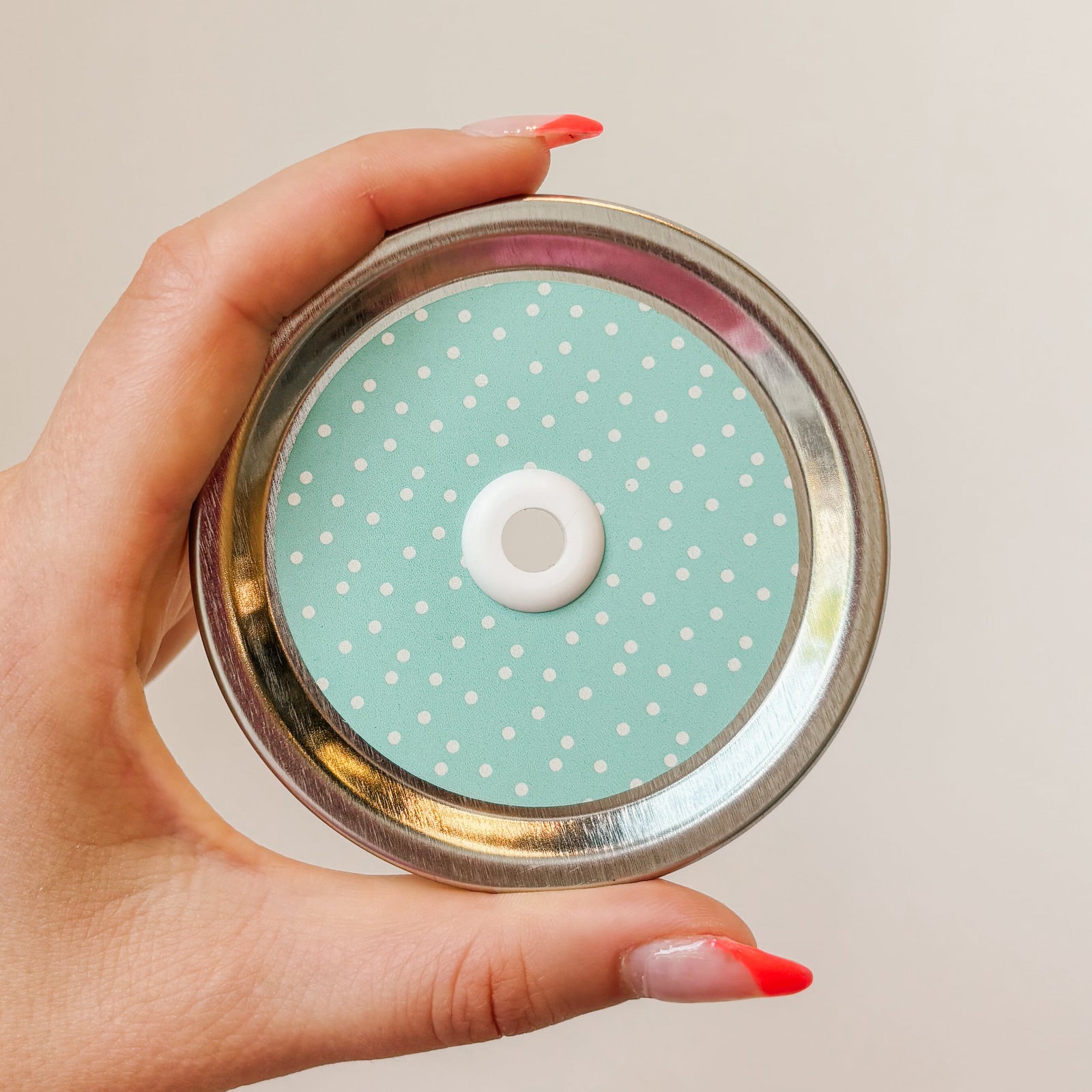 Hand holding a mason jar patterned straw lid that has small white polka dots on a teal background.