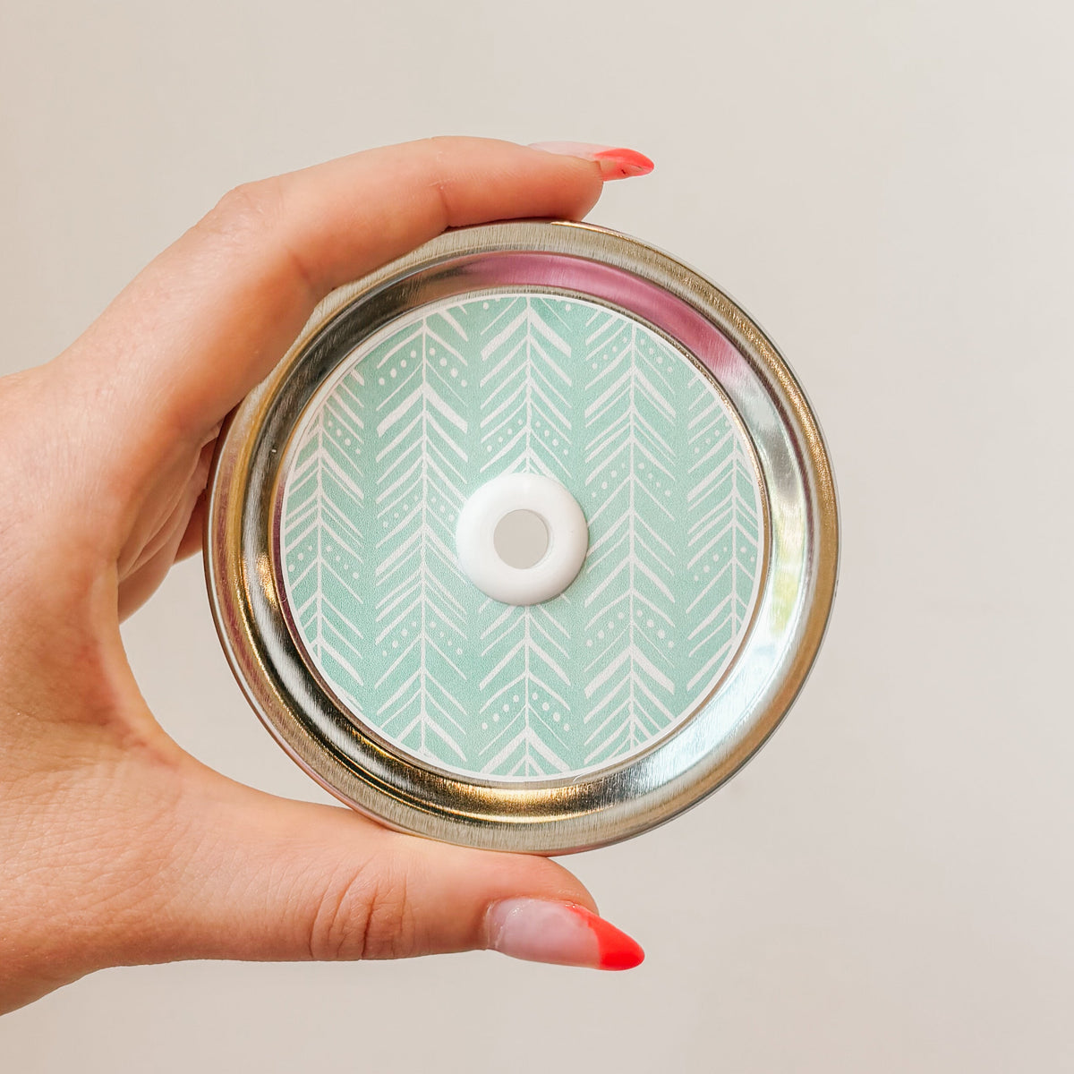Hand holding a mason jar patterned straw lid with white boho style chevron pattern on a light aqua background