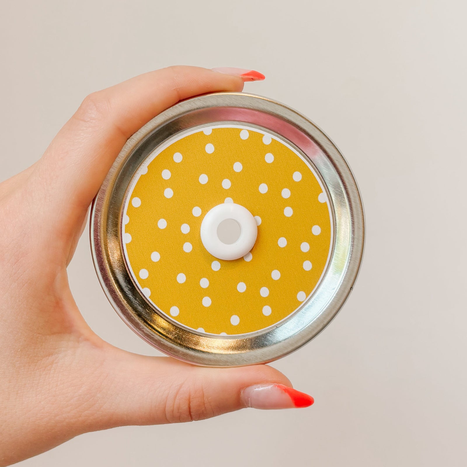 Hand holding a wide mouth mason jar pattern straw lid. White polka dots wiht a mustard yellow background.