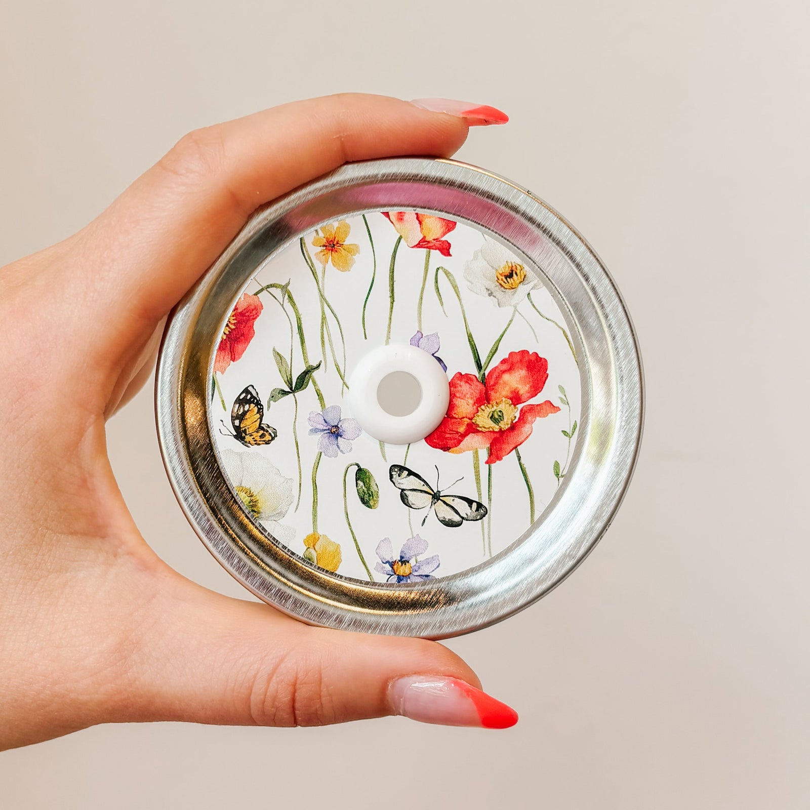 straw lid with a white background, there are green stems/leaves taking up most of the centre of the lid, there are also flowers and butterflies scattered