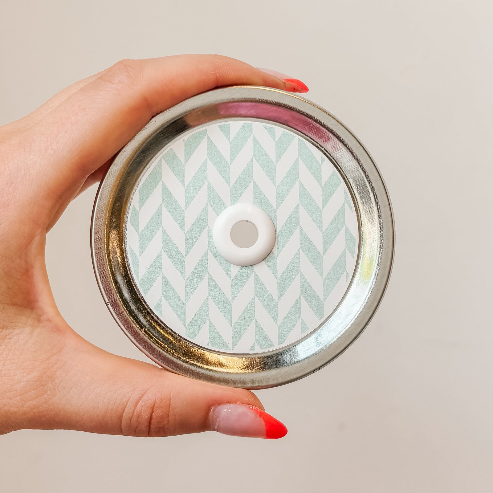Hand holding mason jar patterned straw lid that has white chevron lines on minty blue background