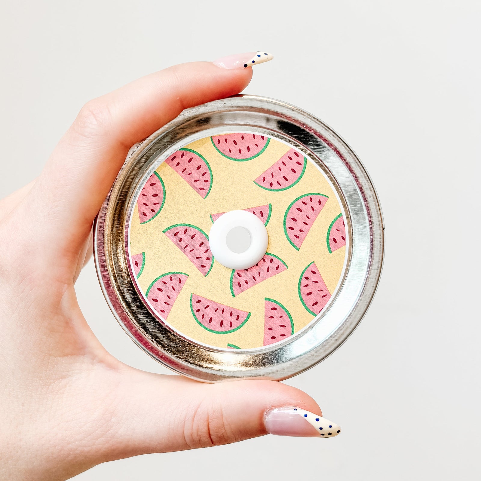 Hand holding mason jar patterned straw lid with watermelon slices on a yellow background