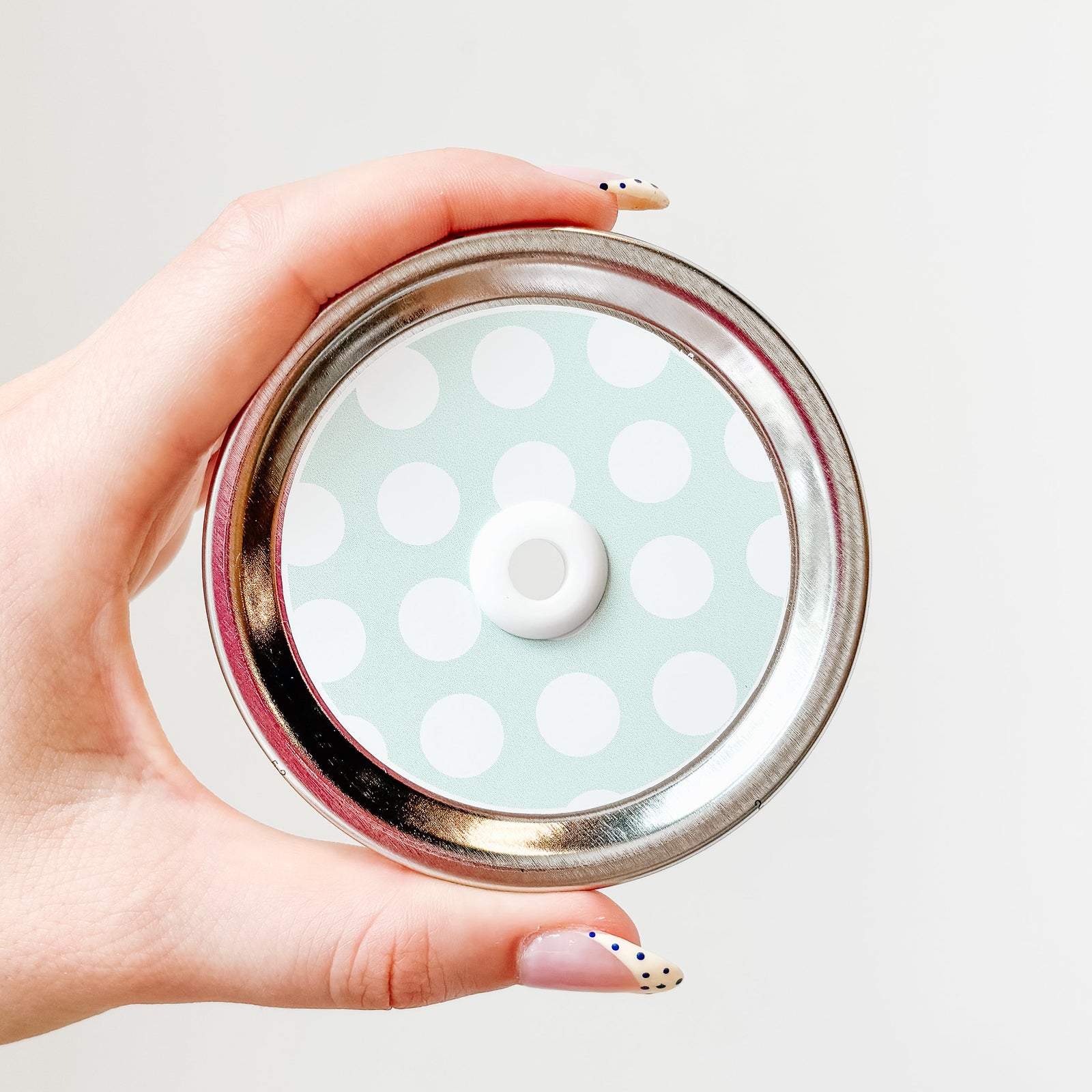 Hand holding mason jar straw lid that has large white polka dots on minty blue background
