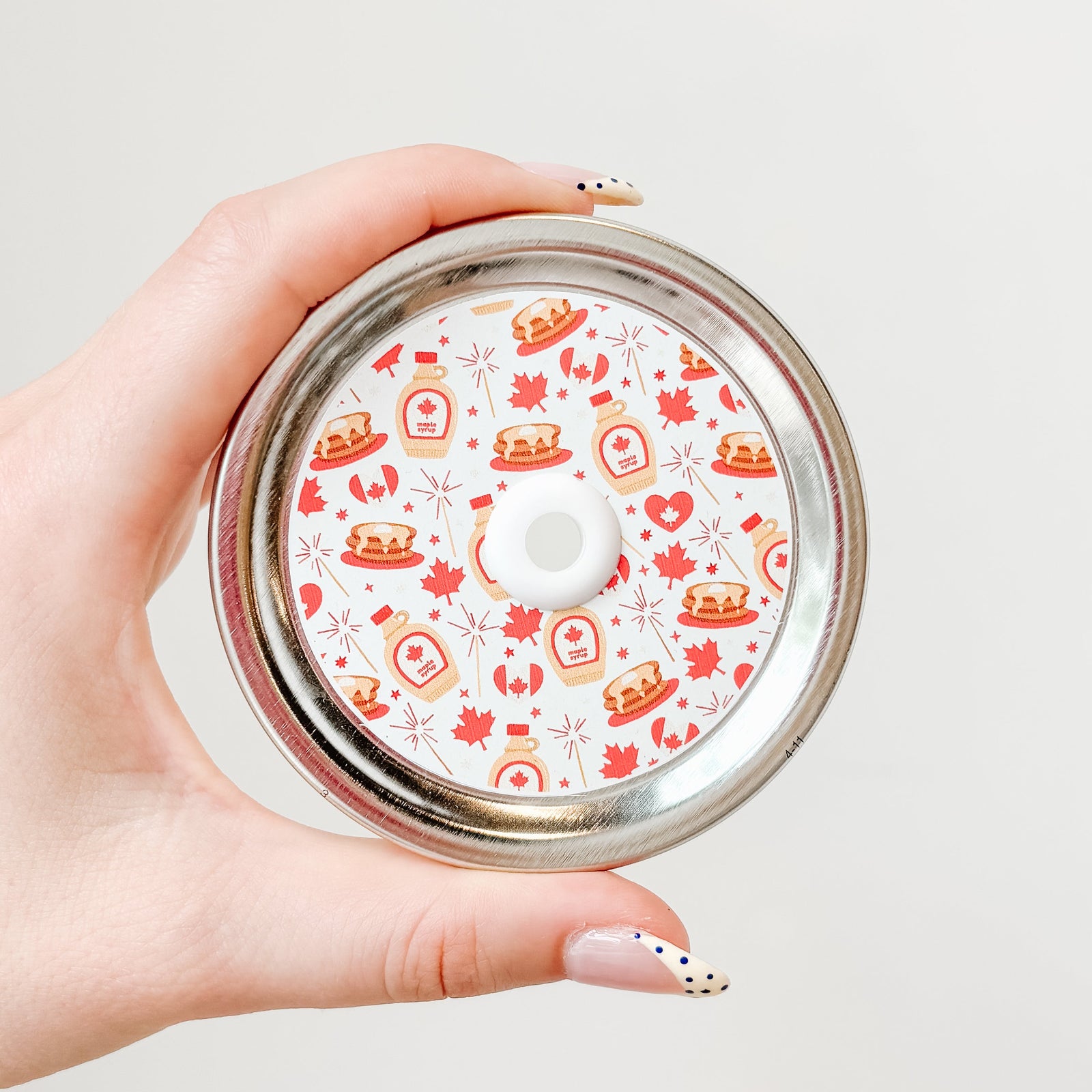 a straw lid that has a white background with maple leafs, canadian flags, pancake stacks, bottles of maple syrup, and fireworks all in a red, brown, and white colour scheme