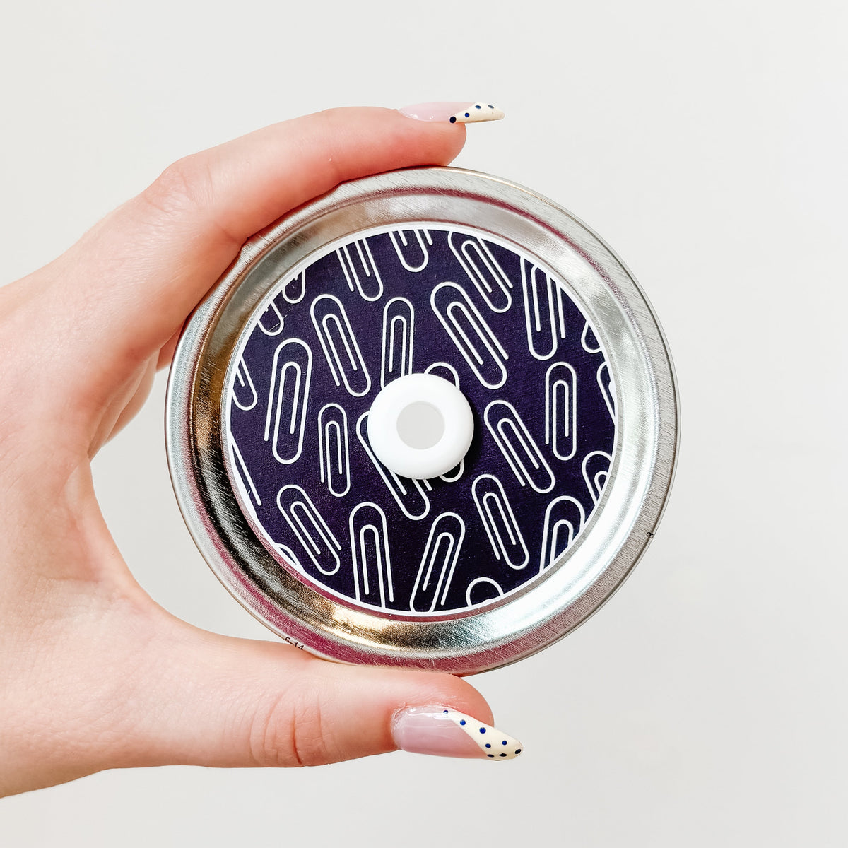 Hand holding a mason jar straw lid with paper clips on a black background