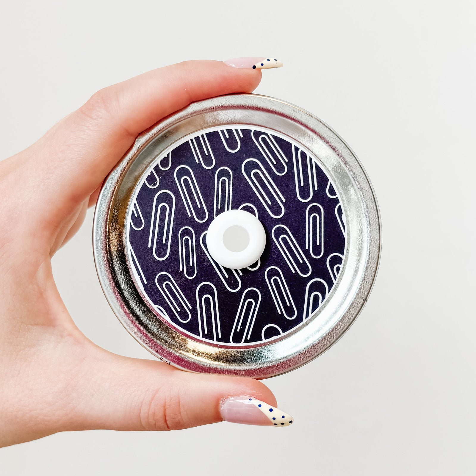 Hand holding a mason jar straw lid with paper clips on a black background
