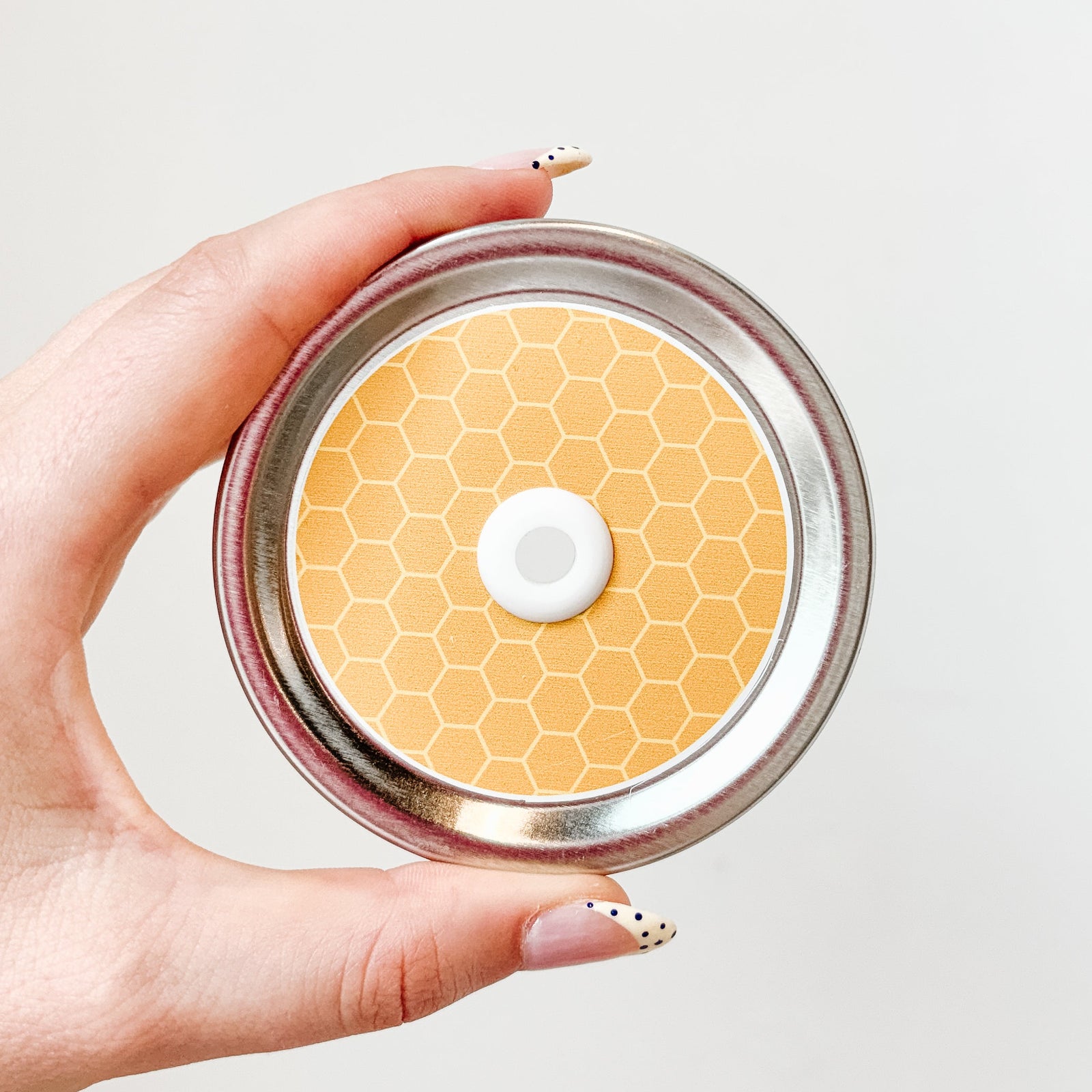 Hand holding mason jar patterned straw lid that is a yellow and orange honeycomb design