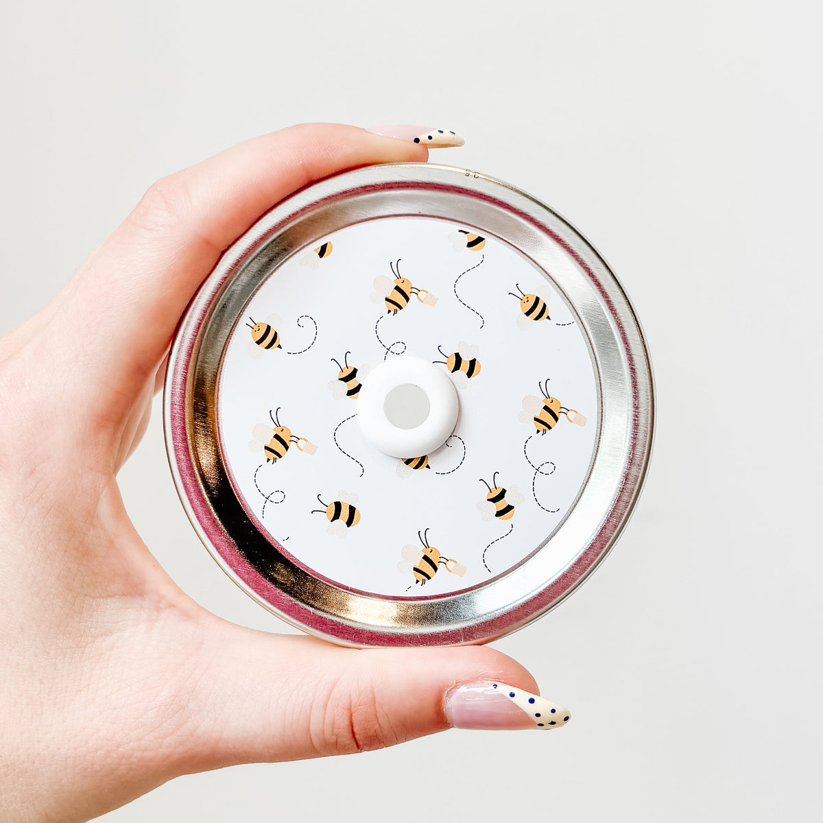 Hand holding a mason jar straw lid that has little bees flying around leaving a trail on white background
