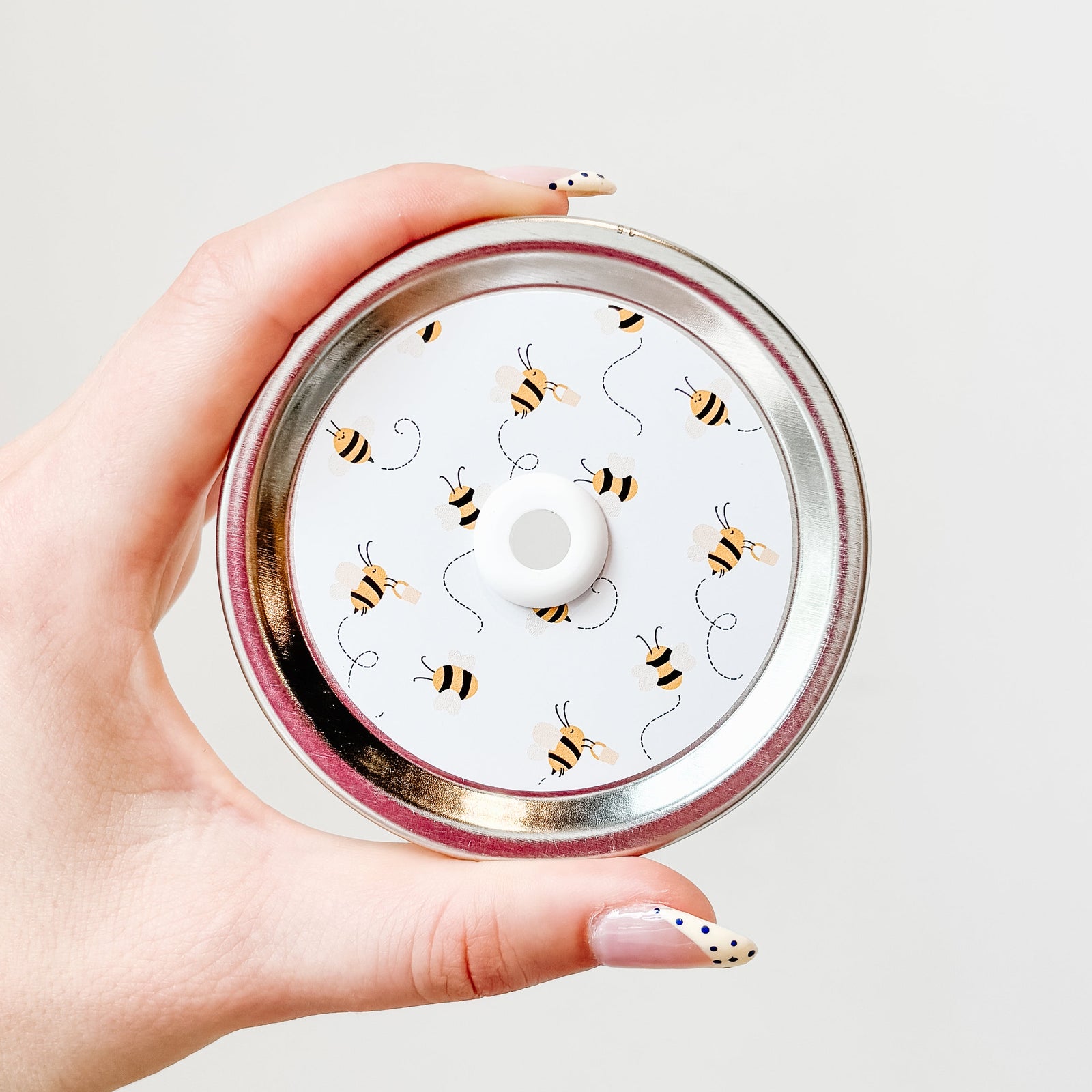 Hand holding a mason jar straw lid that has little bees flying around leaving a trail on white background