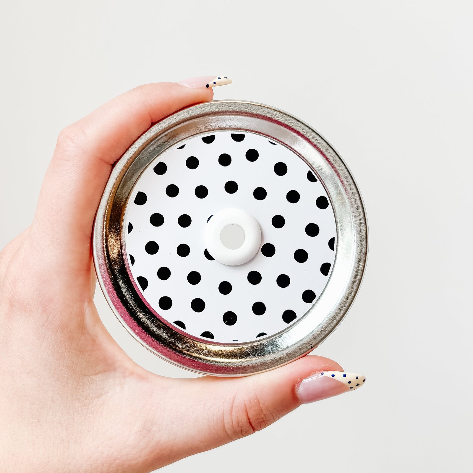 Hand holding mason jar straw lid with black polka dots and white background