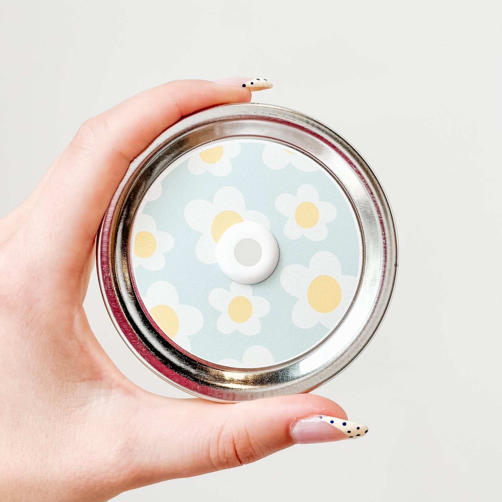 Hand holding mason jar straw lid that has big daisies on light blue background