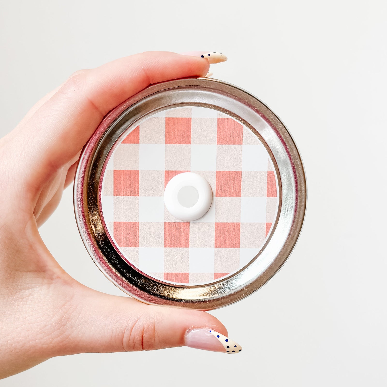 Hand holding mason jar straw lid with large white and peach gingham design