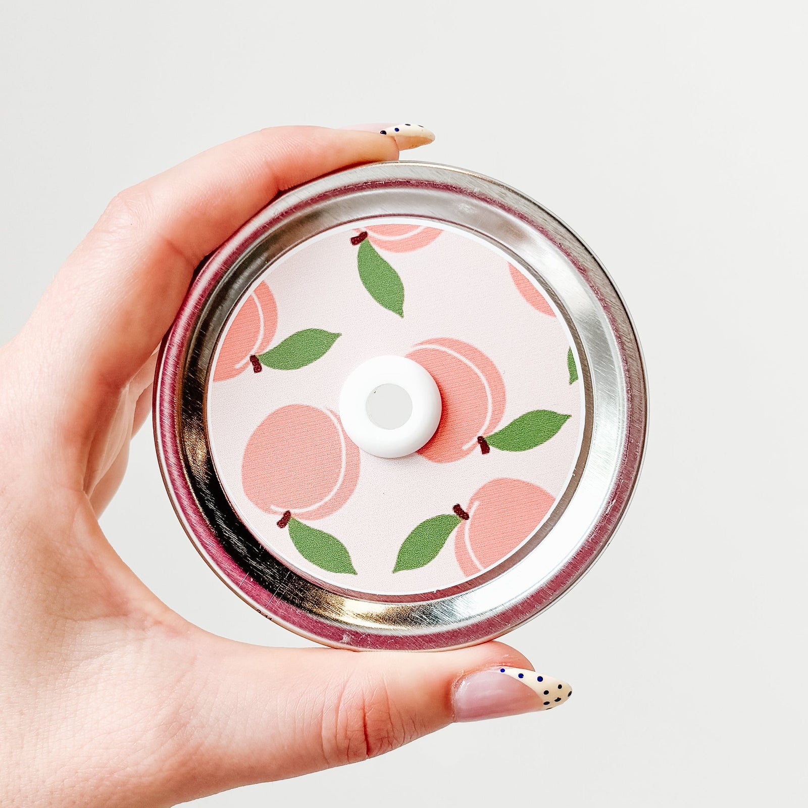 Hand holding patterned mason jar straw lid that has peaches on pale pink background