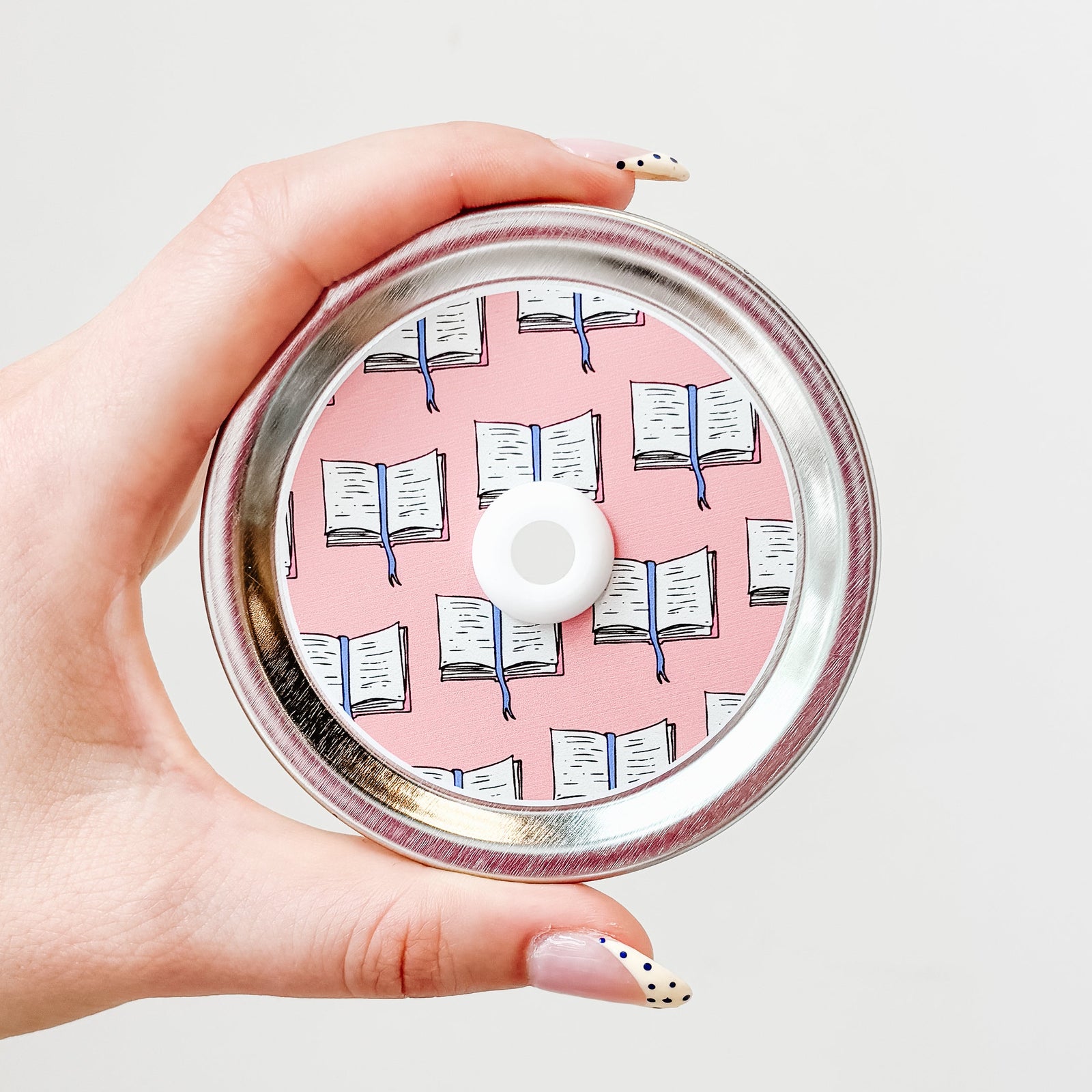 straw lid with light pink background, repeated pattern of an open book with a blue ribbon bookmark