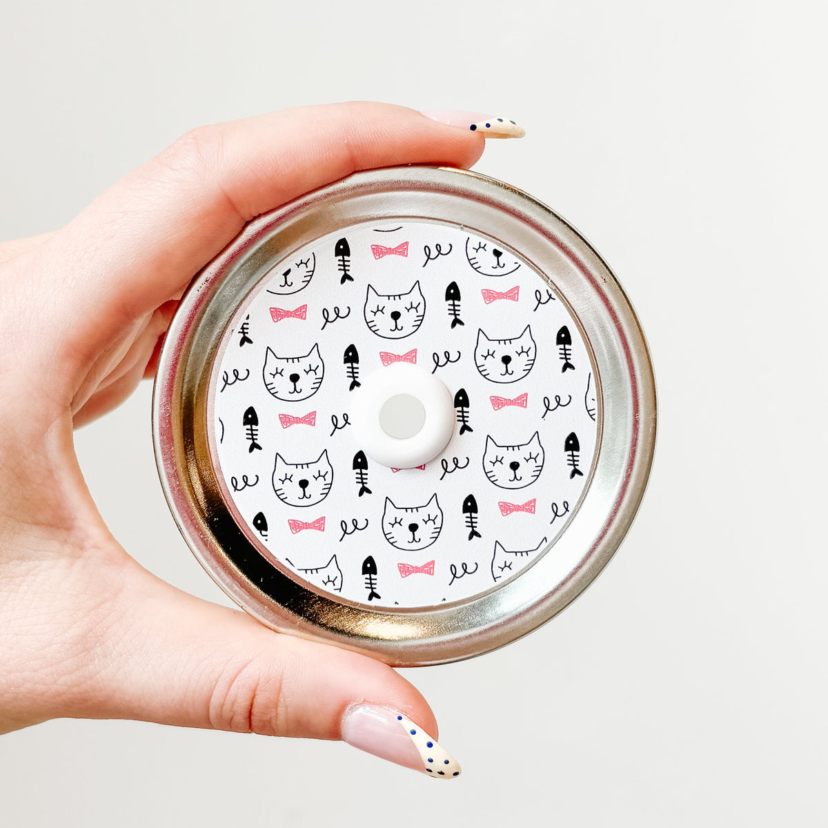 straw lid with white background, line drawings of cat faces, fish skeletons, and pink bow ties