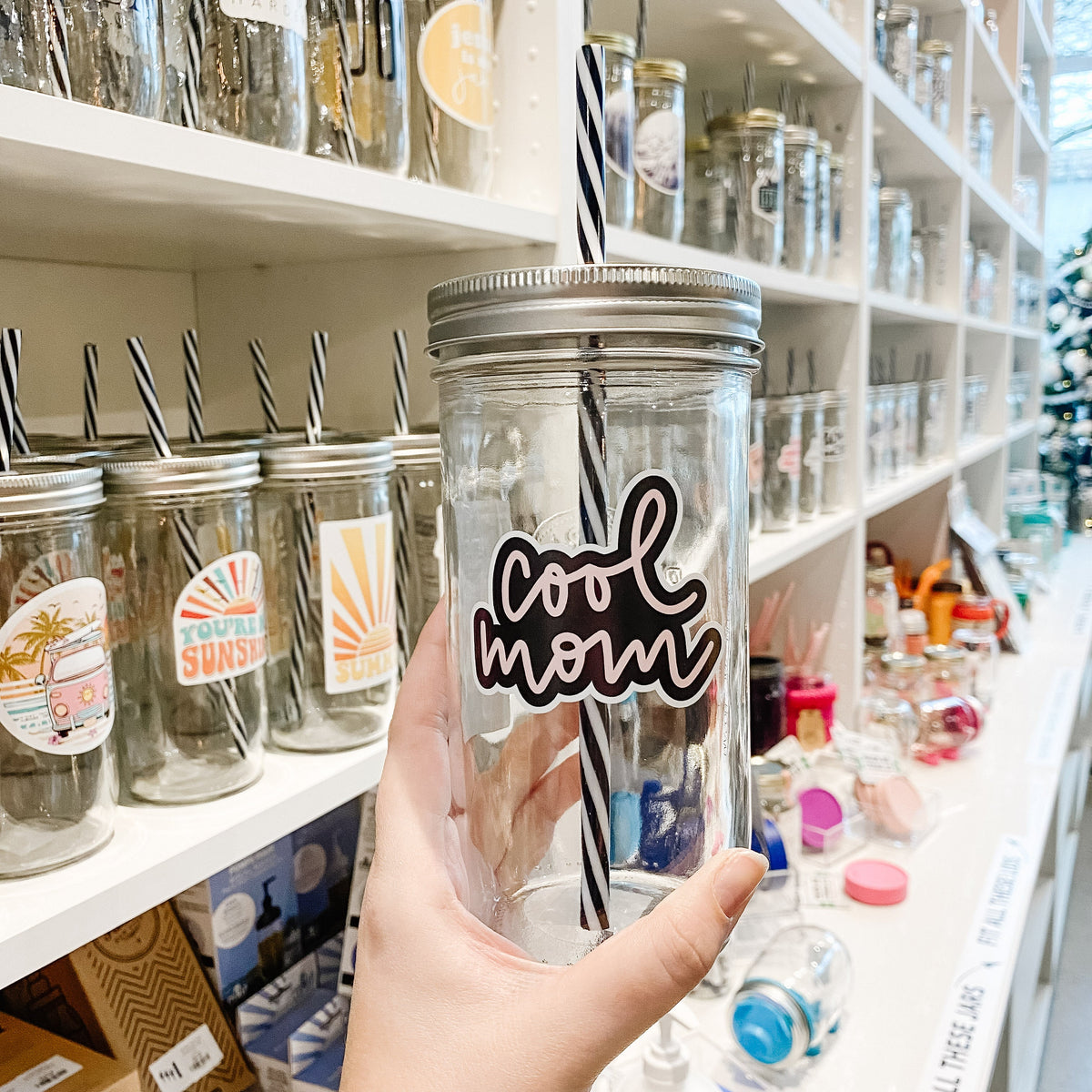 Hand holding a mason jar tumbler that says “cool mom” in pink script on a black background
