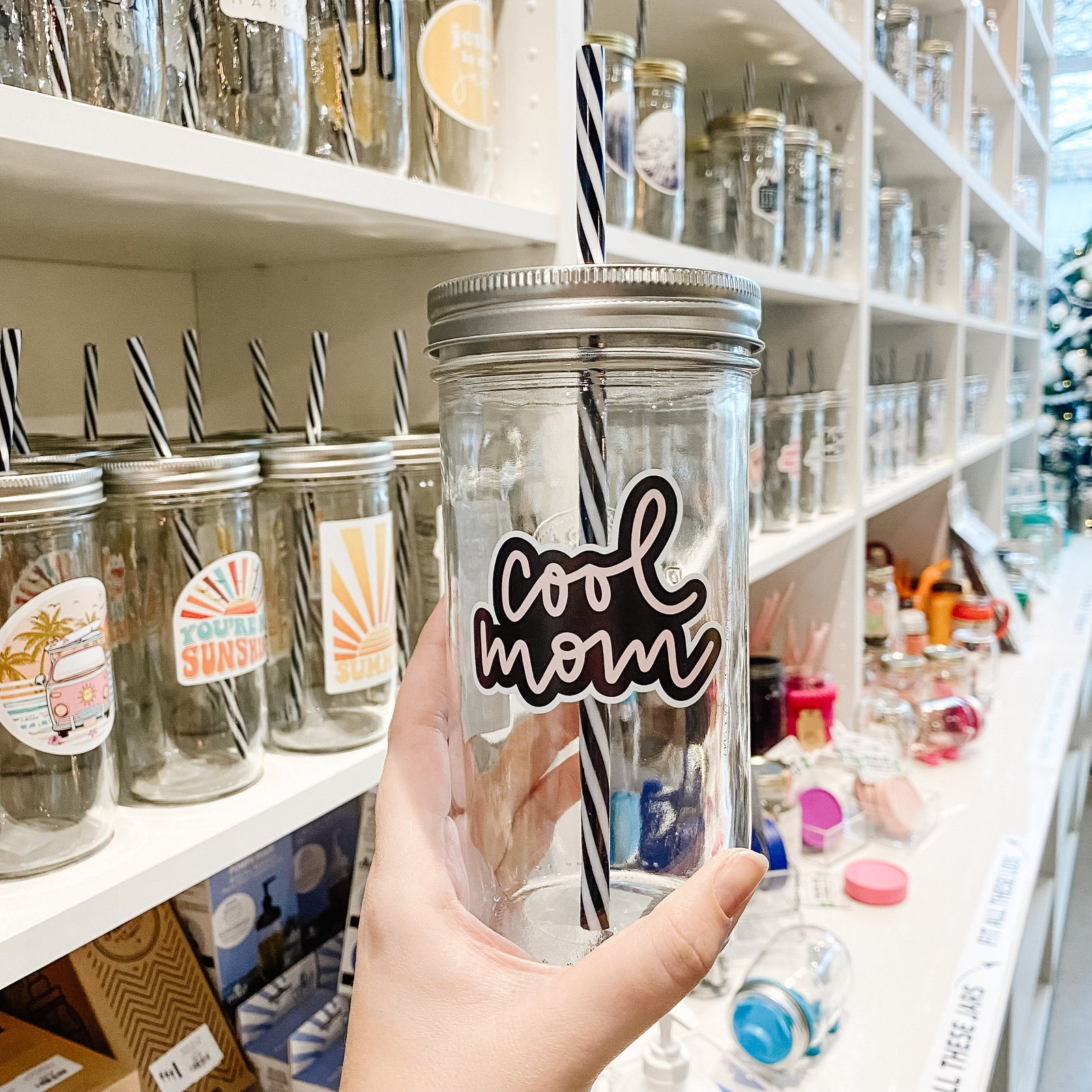 Hand holding a mason jar tumbler that says “cool mom” in pink script on a black background