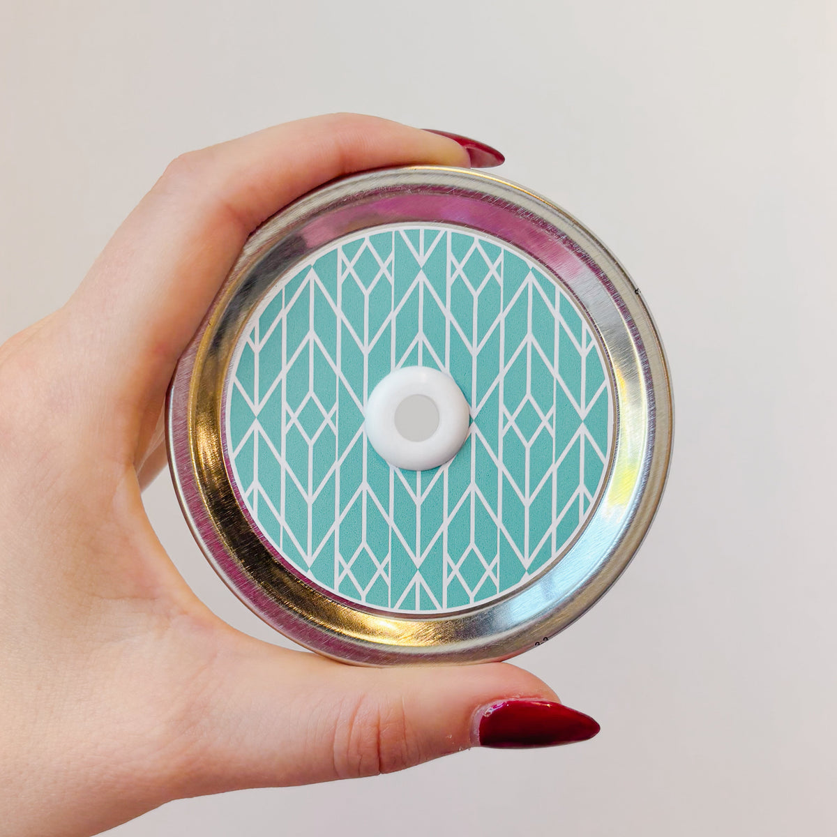 hand holding mason jar straw lid that has white line geometric design on teal background. 