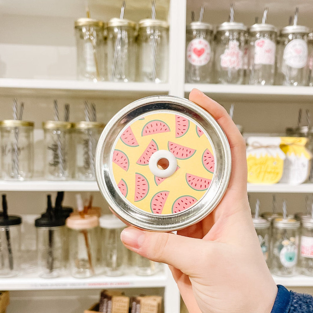 Hand holding mason jar patterned straw lid with watermelon slices on a yellow background