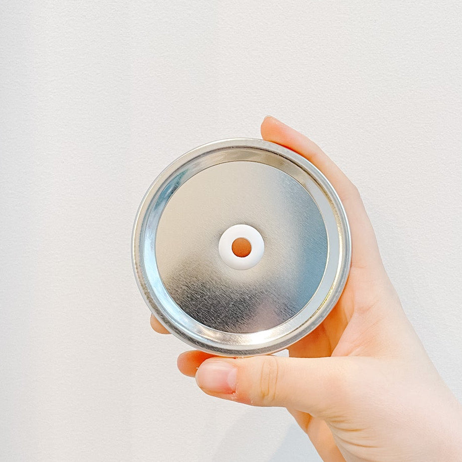 Hand holding a plain silver mason jar straw lid on white background 