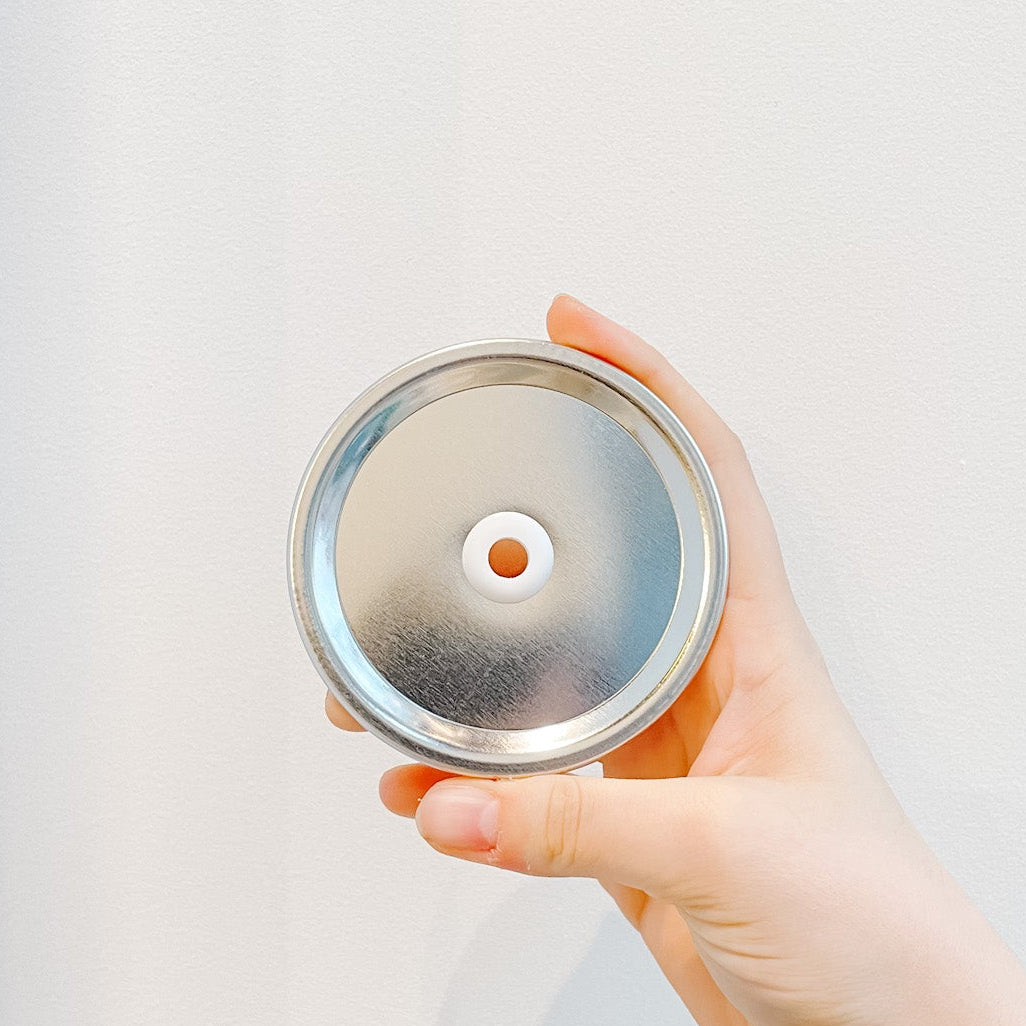 Hand holding a plain silver mason jar straw lid on a white background 
