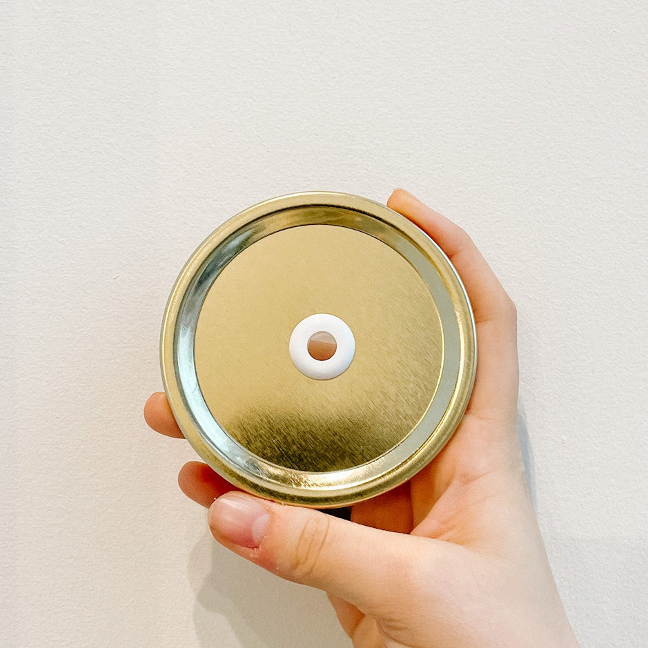 Hand holding a plain gold mason jar straw lid with white background 