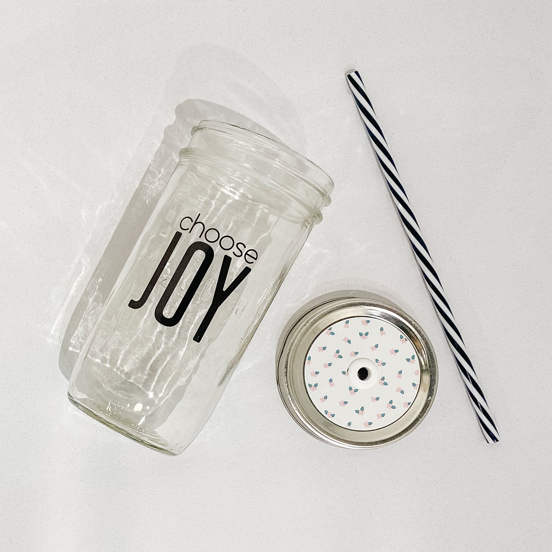 Hand holding a mason jar tumbler that reads choose joy in black text on clear background 