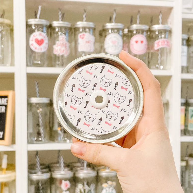 Hand holding mason jar patterned straw lid with cats, fish bones and pink bows