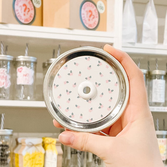 Hand holding mason jar patterned straw id that has tiny pink flowers on off white background 