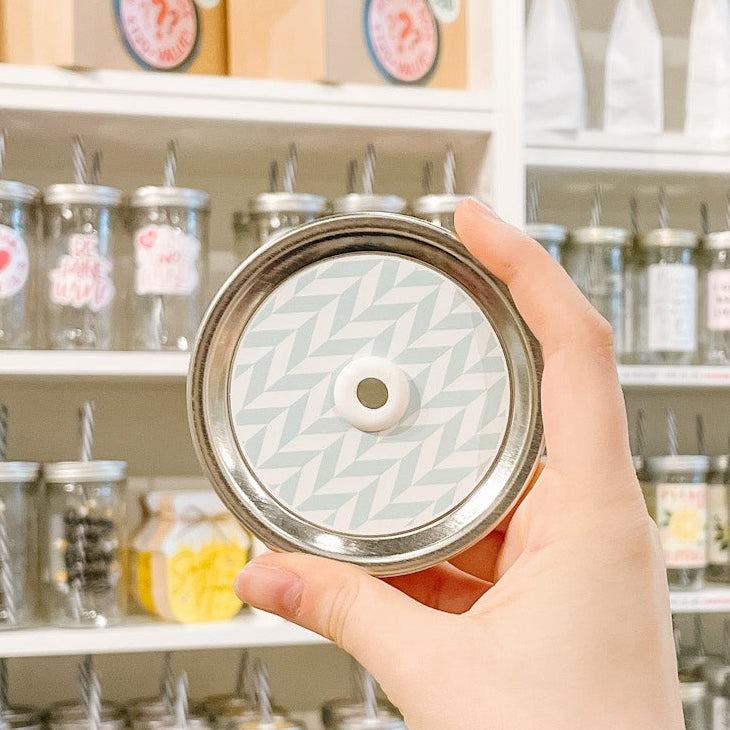 Hand holding mason jar patterned straw lid that has white chevron lines on minty blue background 